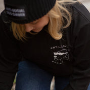 Person wearing a black jacket with 'Anti-Social' design and a black beanie outdoors.